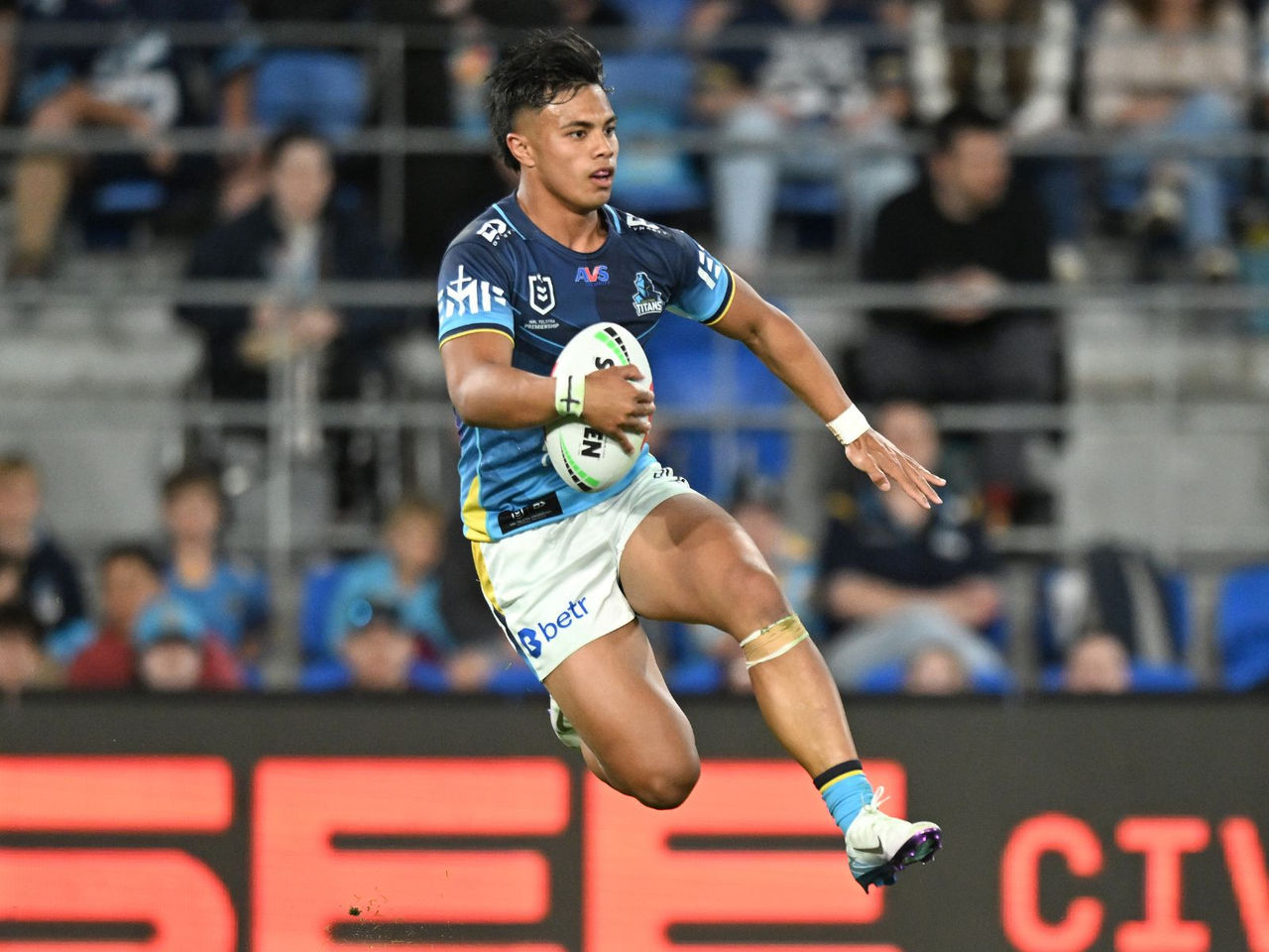 NRL Gold Coast Titans player holding the ball jumping in the air